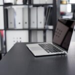 Ordinateur portable allumé sur un bureau noir avec étagères de rangement en arrière-plan
