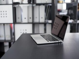 Ordinateur portable allumé sur un bureau noir avec étagères de rangement en arrière-plan