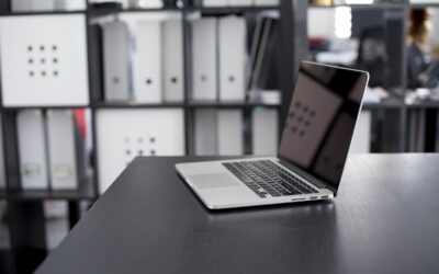 Ordinateur portable allumé sur un bureau noir avec étagères de rangement en arrière-plan