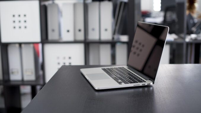 Ordinateur portable allumé sur un bureau noir avec étagères de rangement en arrière-plan