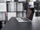 Ordinateur portable allumé sur un bureau noir avec étagères de rangement en arrière-plan