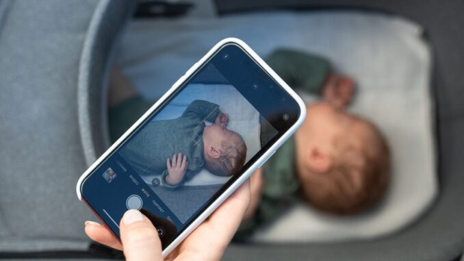 Main tenant smartphone montrant photo d'enfant endormi dans lit d'enfant
