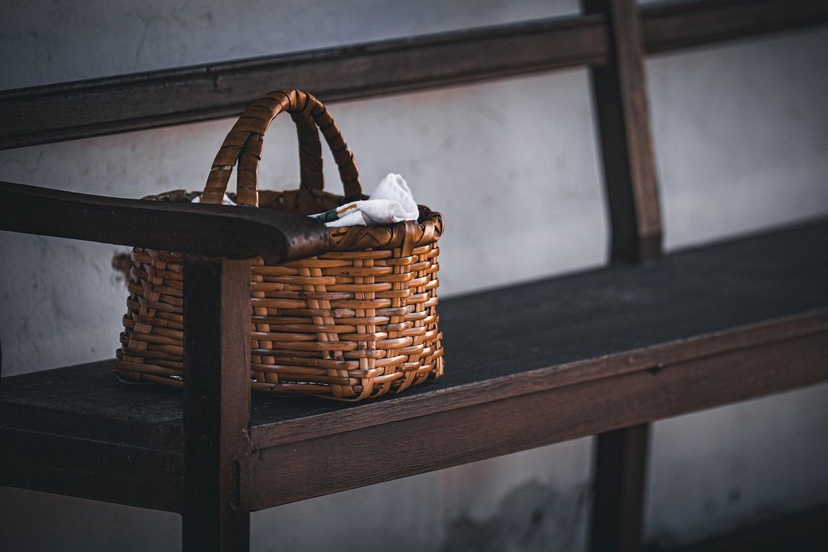 Panier en osier posé sur un banc en bois, contenant un objet blanc, contre un mur gris Panier en osier posé sur un banc en bois, contenant un objet blanc, contre un mur gris