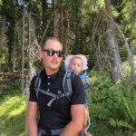 Un homme avec lunettes noires porte un bébé dans un sac dorsal