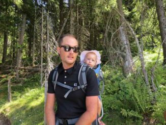 Un homme avec lunettes noires porte un bébé dans un sac dorsal