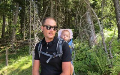 Un homme avec lunettes noires porte un bébé dans un sac dorsal