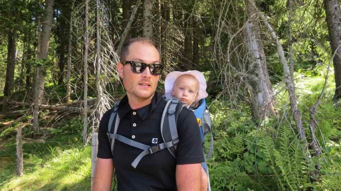 Un homme avec lunettes noires porte un bébé dans un sac dorsal