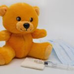 Un ours en peluche jaune à côté d'une seringue et d'un masque