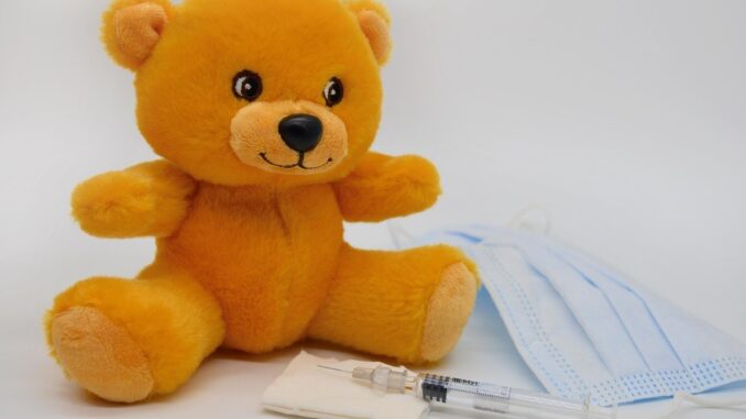 Un ours en peluche jaune à côté d'une seringue et d'un masque